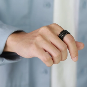 Gros plan d'une bague large en acier noir mat avec texture de bracelet sur l'index