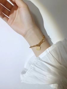 Bracelet à maillons trombones dorés avec pendentif carré porté par un mannequin