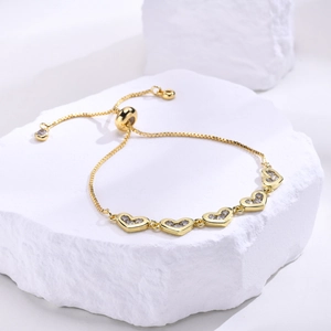 Detail of adjustable gold heart bracelet with zircon pavé on white stone platform