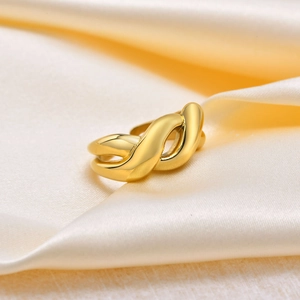 Detailed close-up of golden twisted knot ring on elegant champagne satin fabric background