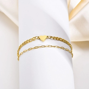 Dettaglio di un bracciale dorato a doppio strato con cuore e catena a maglie piatte