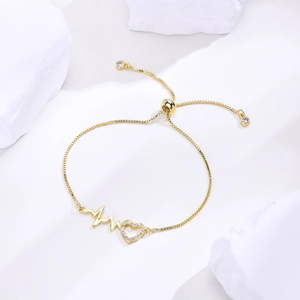 Detailed close-up of a gold adjustable bracelet with a zircon heart and heartbeat motif