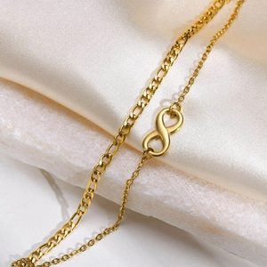 Dettaglio della collana infinity dorata con catena figaro su marmo bianco e seta