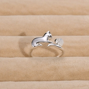 Macro detail of silver cat ring catching a round moonstone on a beige velvet display