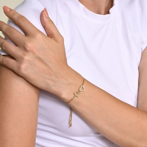 Close-up of golden EKG heartbeat bracelet with sparkling zircon heart on model wrist