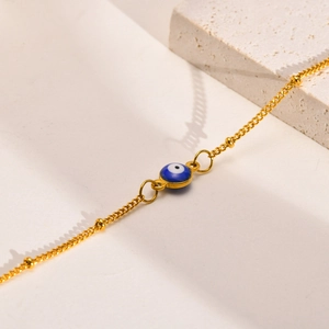 Détail d'un bracelet doré à perles avec pendentif œil protecteur bleu sur fond pierre