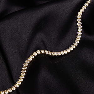 Makroaufnahme einer goldenen Tenniskette mit Zirkonia-Steinen auf schwarzer Seide
