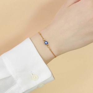 Bracelet élégant en chaîne dorée avec pendentif œil bleu porté au poignet