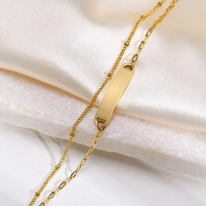Dettaglio di un bracciale dorato a doppio strato con barra rettangolare lucida e maglie a sfera