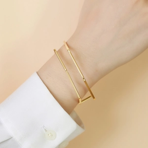 Polished gold minimalist C-shaped geometric bracelet worn on a female wrist over a white sleeve