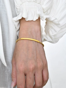 Détail d'un bracelet torsadé doré avec plaque lisse porté par un mannequin sur le poignet