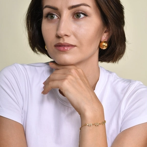 Golden leaf bracelet with zircon stones and ball earrings worn by a model