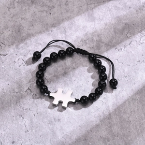 Detail of adjustable black beaded bracelet featuring a polished silver puzzle piece charm