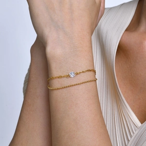 Dettaglio di un bracciale dorato a doppio strato con zircone e catena a sfere al polso
