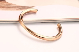 Detail of rose gold open cuff bangle with a high-polished mirror finish on a magazine