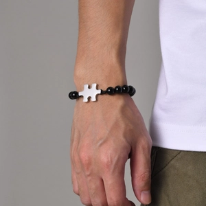 Detailed shot of black beaded braided bracelet with a polished silver puzzle piece on a wrist