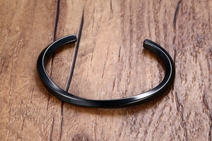 Macro detail of black twisted minimalist stainless steel cuff bangle on wood