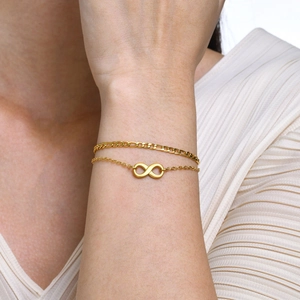 Primo piano di un bracciale dorato a doppio strato con simbolo infinito al polso di donna