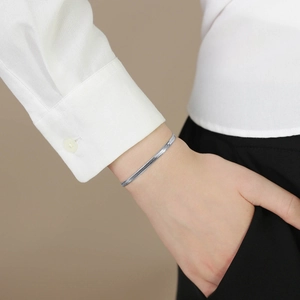 Close-up of a silver flat snake chain bracelet worn with a professional white shirt