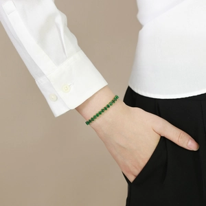 Nahaufnahme eines goldenen Tennisarmbands mit ovalen grünen Zirkonia am Handgelenk