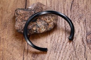 Polished black stainless steel cuff bangle on natural stone and wooden background