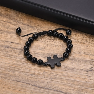 Detail of adjustable black agate beaded bracelet with puzzle piece charm on wood surface