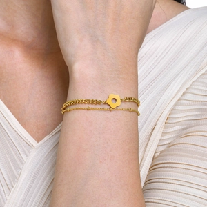 Dettaglio del bracciale dorato a doppio strato con ciondolo a fiore su polso di modella
