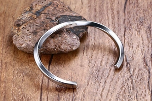 Close-up of polished stainless steel twisted open bangle on rustic stone and wood base