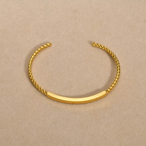 Détail d'un bracelet ouvert doré au design torsadé avec une barre centrale polie