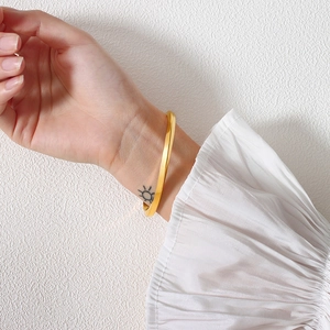 Detail of a minimalist gold twisted cuff bracelet worn on wrist against white fabric