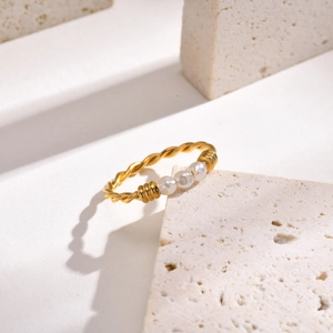 Détail d'une bague torsadée dorée ornée de trois perles sur un support en travertin