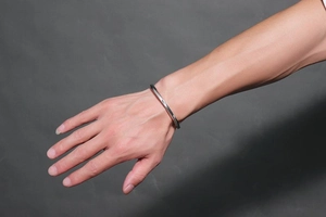 Detail of twisted stainless steel cuff bracelet on a male wrist with polished finish