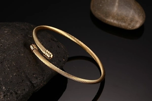Detail of gold cable-knit titanium steel open cuff bracelet on volcanic stone base