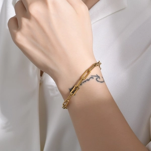 Detail of a minimalist gold paperclip chain bracelet worn on wrist against white fabric