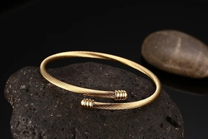 Detail shot of a golden twisted cable open bangle resting on black volcanic stone