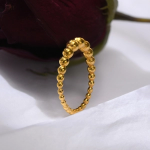 Close-up of golden beaded eternity ring next to a deep red rose on a white surface