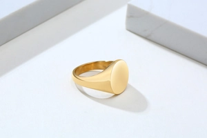 Macro view of a polished 18K gold stainless steel signet ring on white stone background