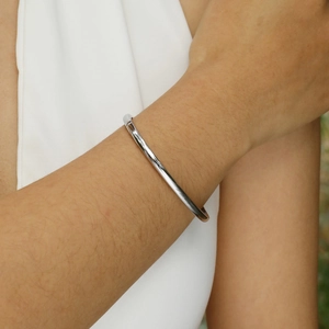 Close-up of minimalist silver stainless steel bangle shown on model wrist with mirror finish