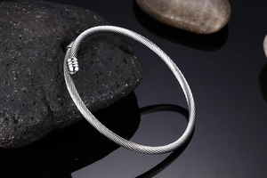 Macro view of silver cable textured steel open bangle on a black stone background