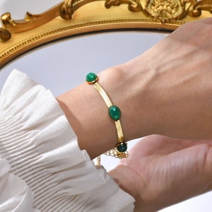 Detailed shot of a gold snake chain bracelet with three oval green zircon gemstones