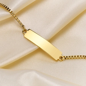 Macro shot of 18K gold box chain bracelet with blank rectangular ID plate on silk