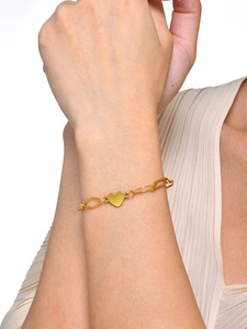 Nahaufnahme eines polierten goldenen Herzanhängers an einem minimalistischen Armband