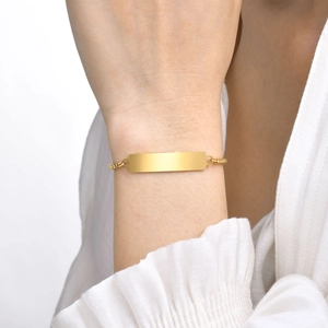 Close-up of a polished gold rectangular bar bracelet on a model's wrist with white sleeve