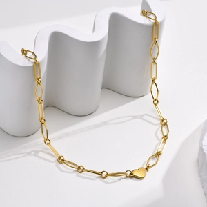 Detail eines goldenen Herzanhängers an einer rechteckigen Gliederkette auf weißem Dekor