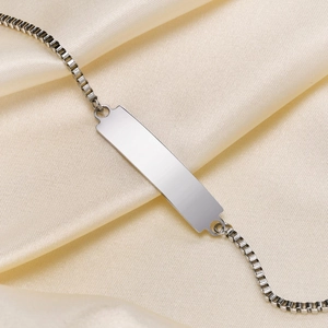 Polished stainless steel box chain ID bracelet on champagne silk fabric close-up