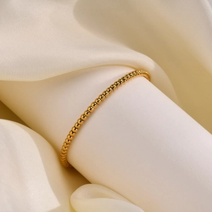 Detailaufnahme eines minimalistischen goldenen Kugelarmbands auf einer weißen Stütze