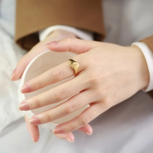 Elegante anello a sigillo in oro con rosa incisa indossato sulla mano di una modella