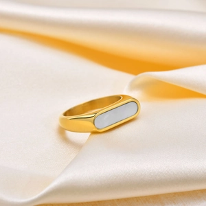 Détail d'une bague géométrique dorée avec nacre blanche sur un fond en soie
