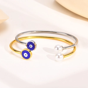 Gold and silver stainless steel evil eye and pearl open bangles on a minimalist display