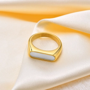 Détail d'une bague géométrique dorée avec incrustation de nacre sur fond de soie beige
